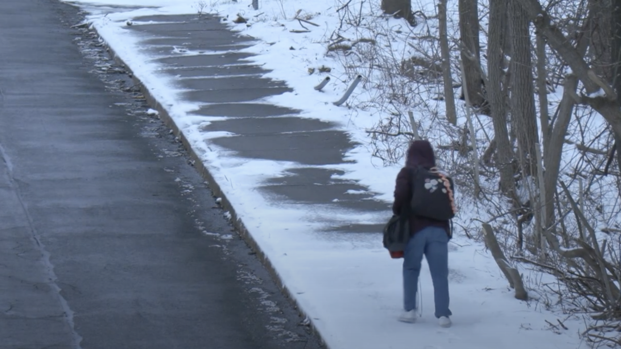 Pedestrians walks up snow covered sidewalk on steep incline.